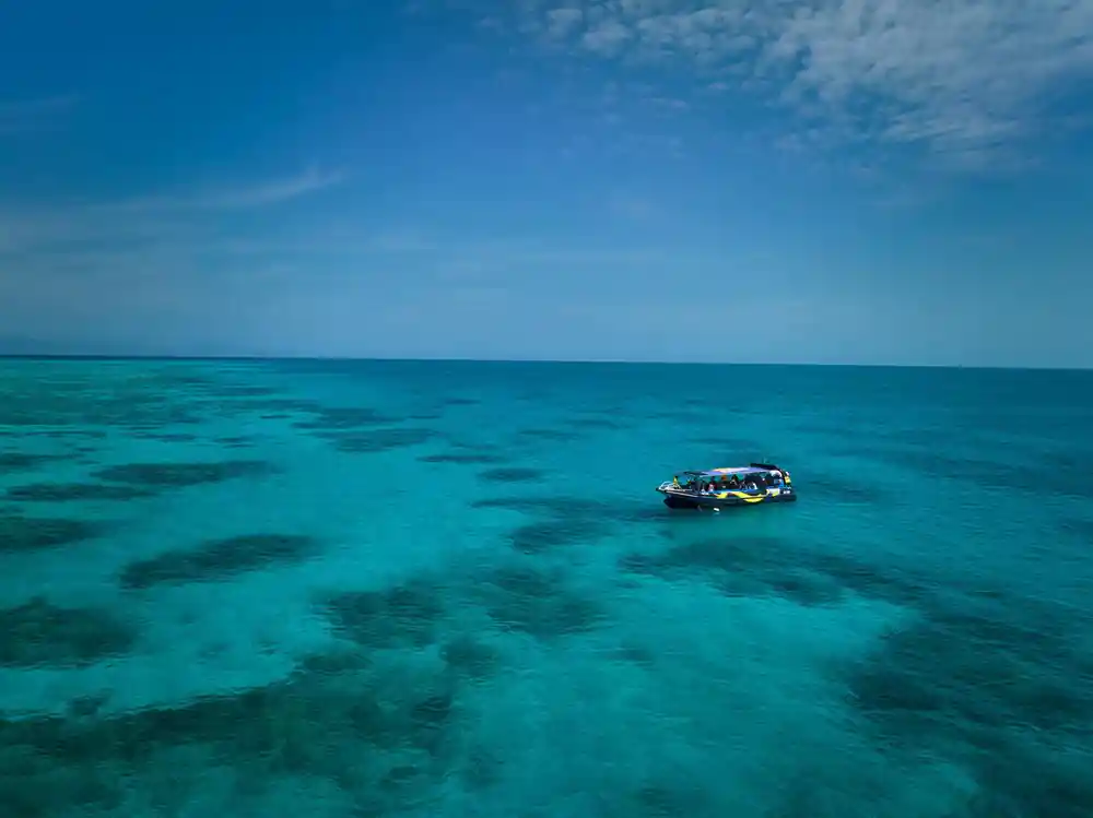 The boat alone on a wide turquoise reef flat under a pale sky