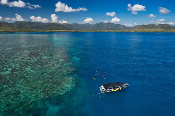 The boat moored over dark reef with snorkellers spread around it, from the air