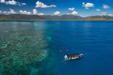 The boat moored over dark reef with snorkellers spread around it, from the air