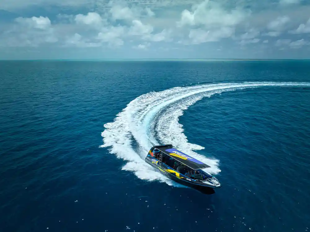 The fast boat carving a curved wake across clear water, from above