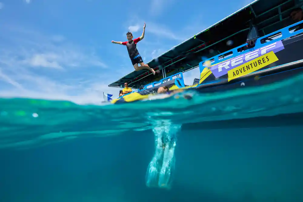 A guest leaping from the boat's rear deck, seen half above and half below the water