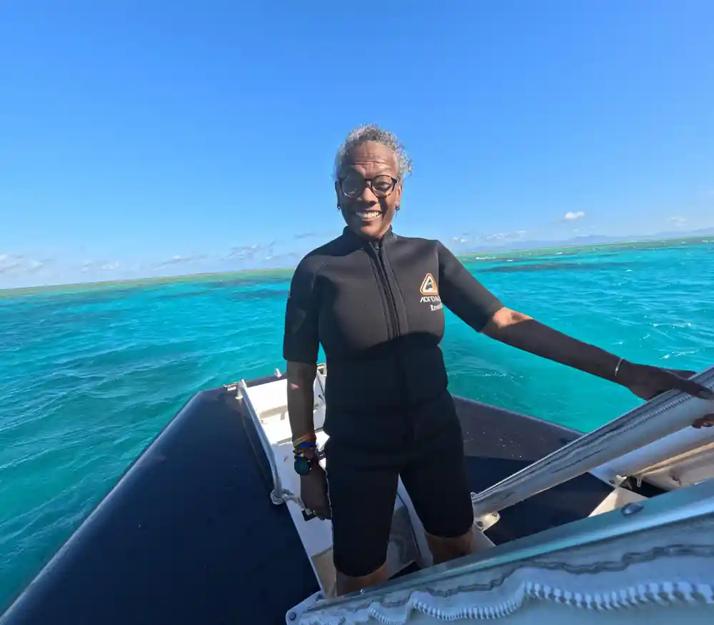 A guest in a wetsuit standing at the boat's rail over turquoise water