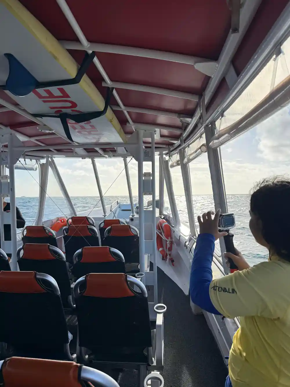 Inside the boat's cabin, seats and a crew member filming at the rail