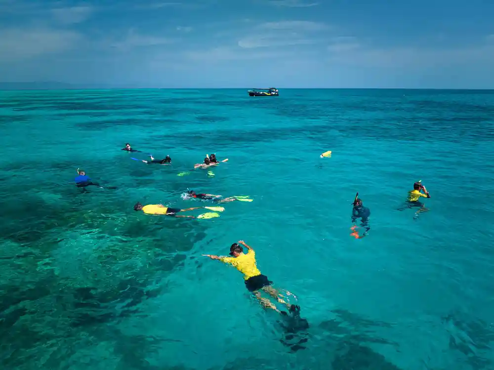 Snorkellers in yellow vests spread across shallow turquoise water