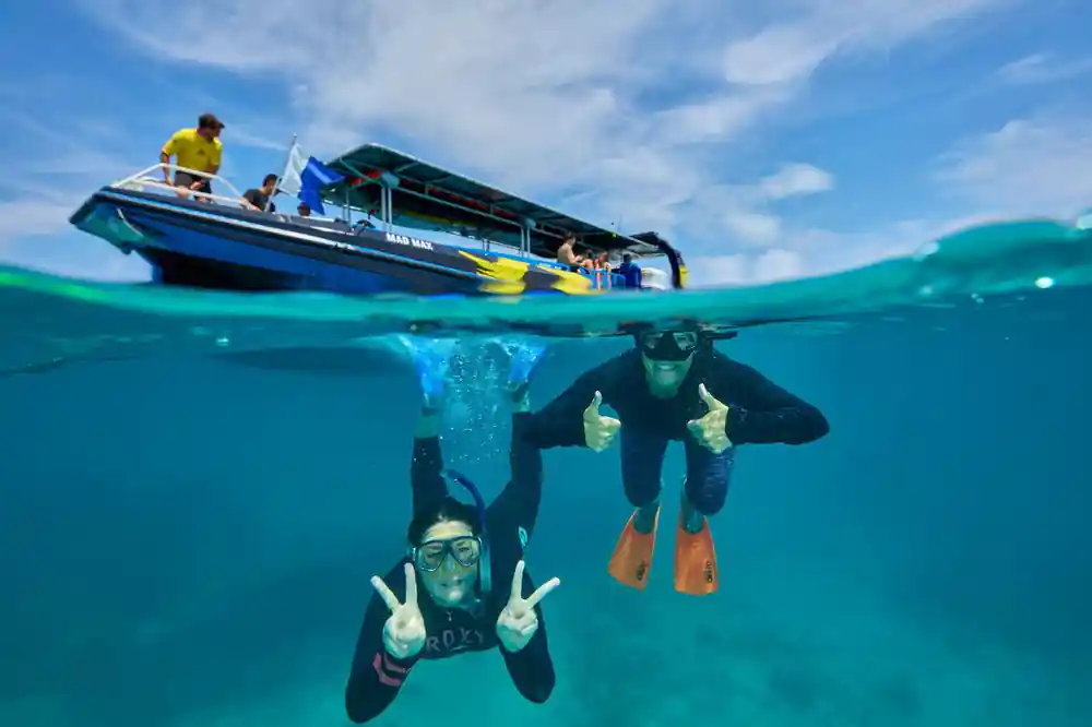 Two snorkellers making peace signs underwater beside the boat